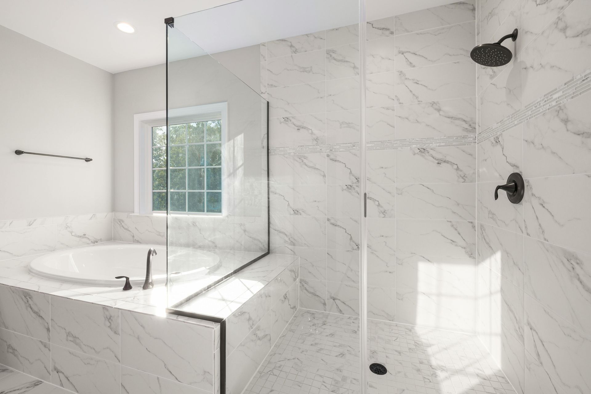 Modern bathroom with marble tile, glass shower, and round tub next to a window.
