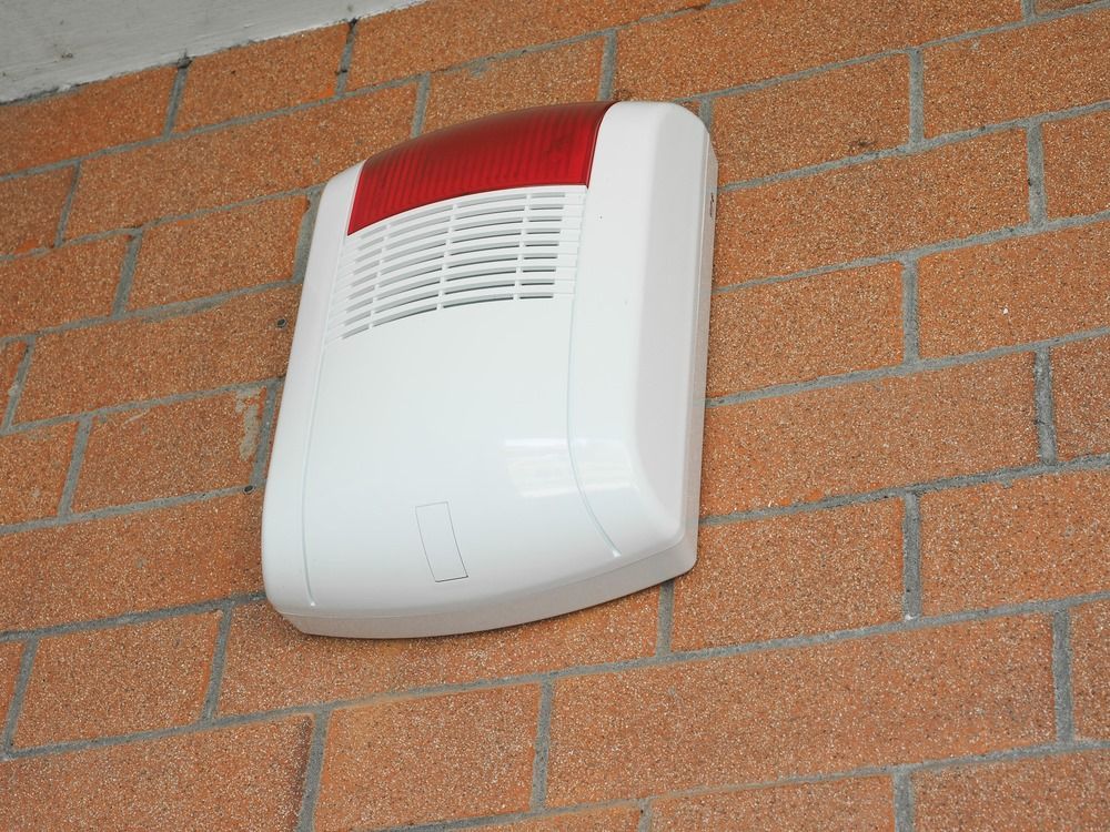 A White and Red Alarm is Mounted on a Brick Wall — Darwin Lock & Key In Coconut Grove, NT