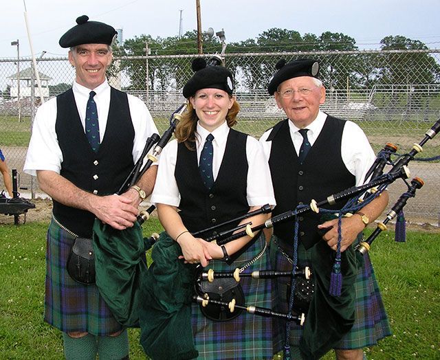 Three men and a woman in kilts holding bagpipes