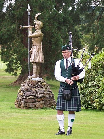 A man in a kilt is playing bagpipes in front of a statue of a knight.