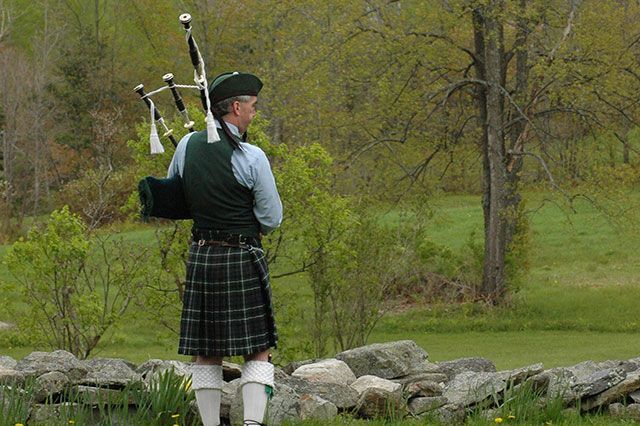 A man in a kilt is playing bagpipes in a field.