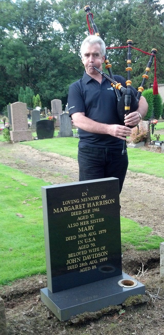 A man is playing a bagpipe in front of a grave.