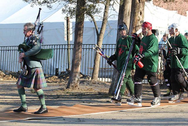 A man in a kilt is playing bagpipes in front of a group of hockey players