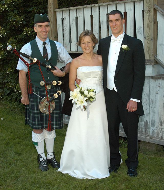 A bride and groom pose with a bagpipe player