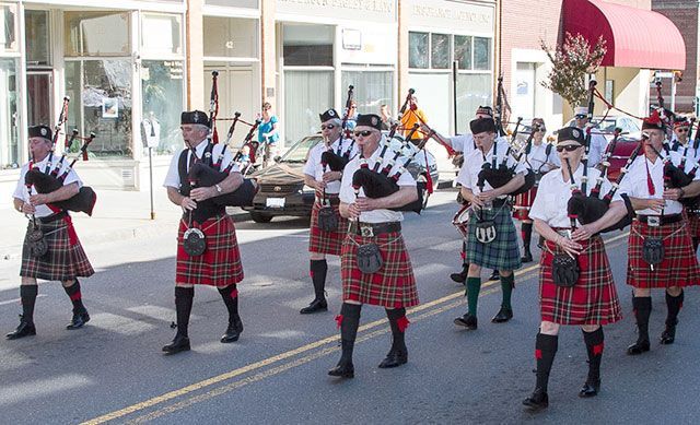 A group of men in kilts are marching down a street playing bagpipes.