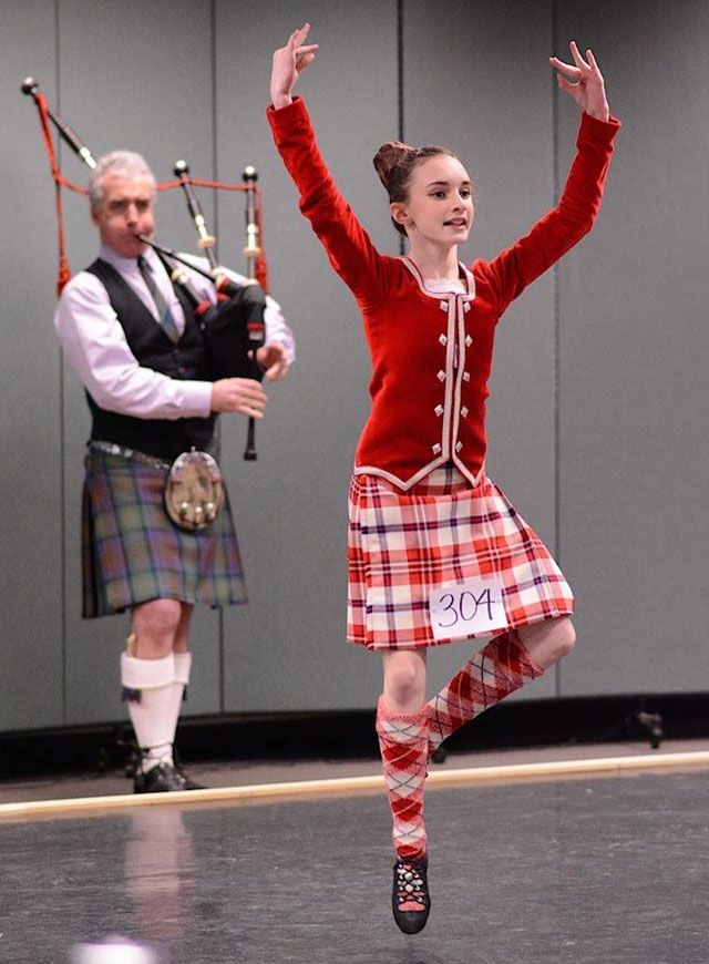 A woman in a kilt is dancing in front of a man playing bagpipes