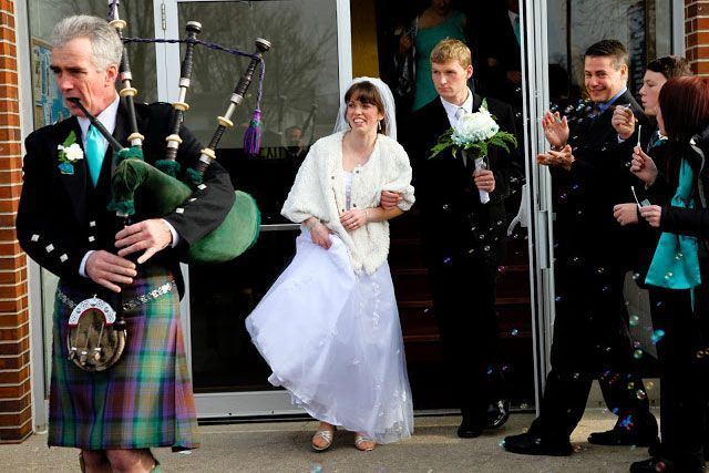 A man in a kilt is playing bagpipes for a bride and groom