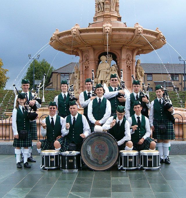 A group of men in kilts pose in front of a fountain