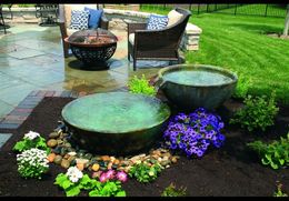 A patio with a fire pit , chairs , flowers and a fountain.