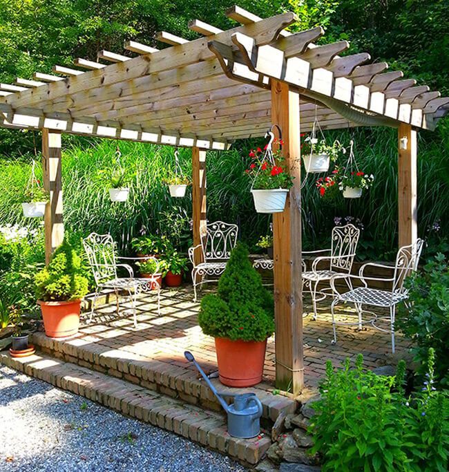 A pergola with chairs and potted plants underneath it