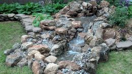 A small waterfall is surrounded by rocks in a backyard.