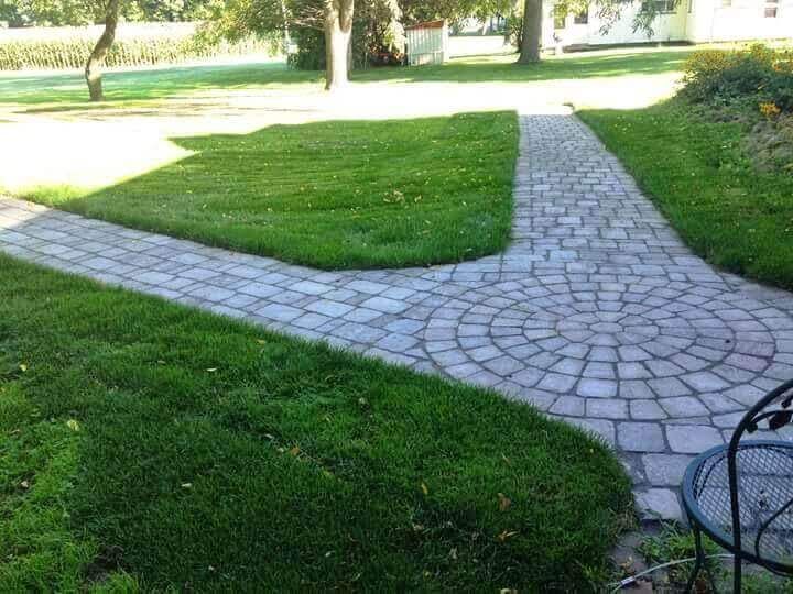 A brick walkway going through a lush green field.