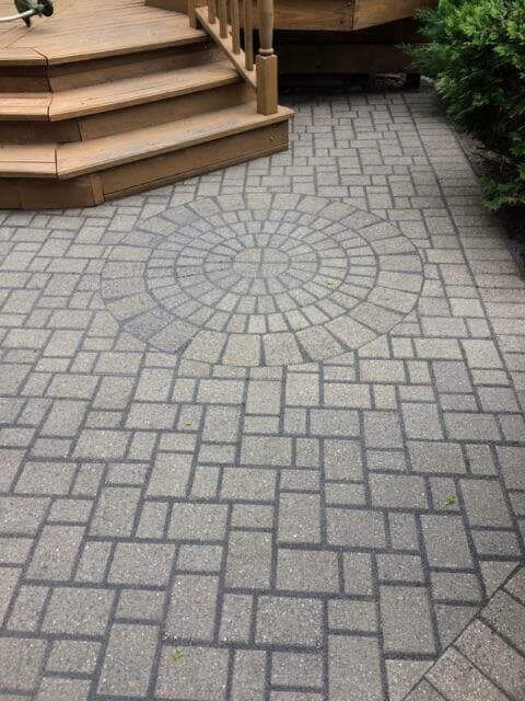 A brick patio with a wooden deck and stairs in the background.