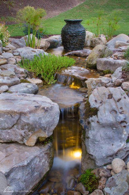 A waterfall surrounded by rocks and a vase in a garden.