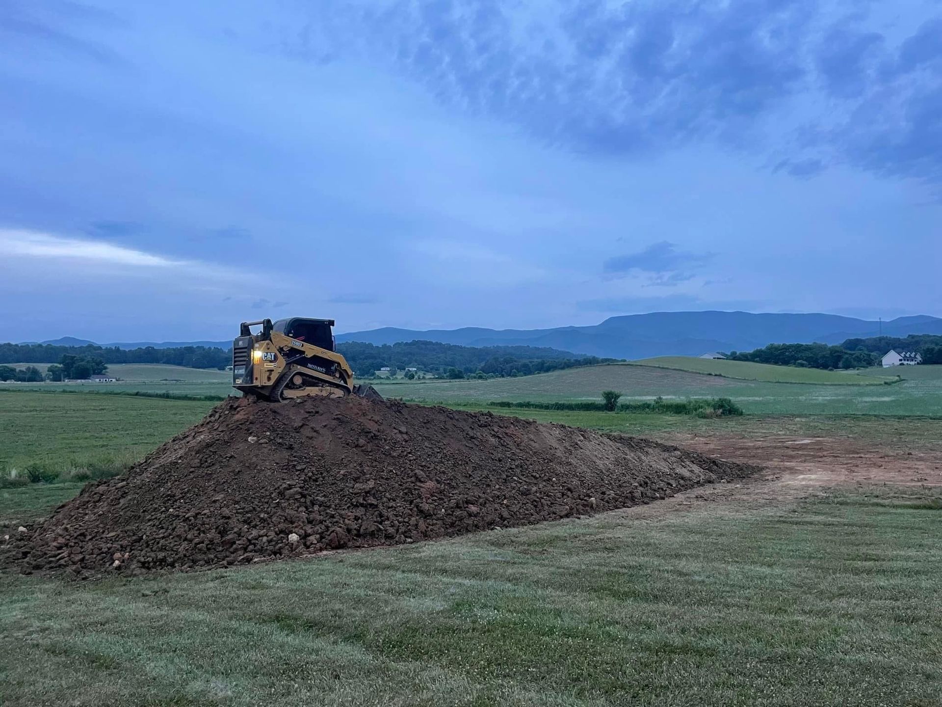 A gravel road going through a grassy field with mountains in the background.