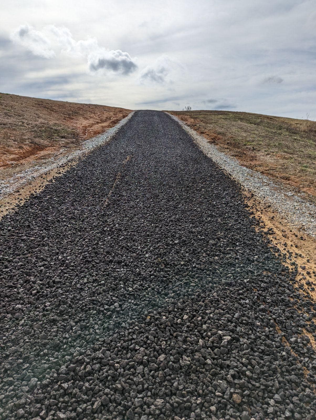 A gravel road going through a field with a hill in the background.