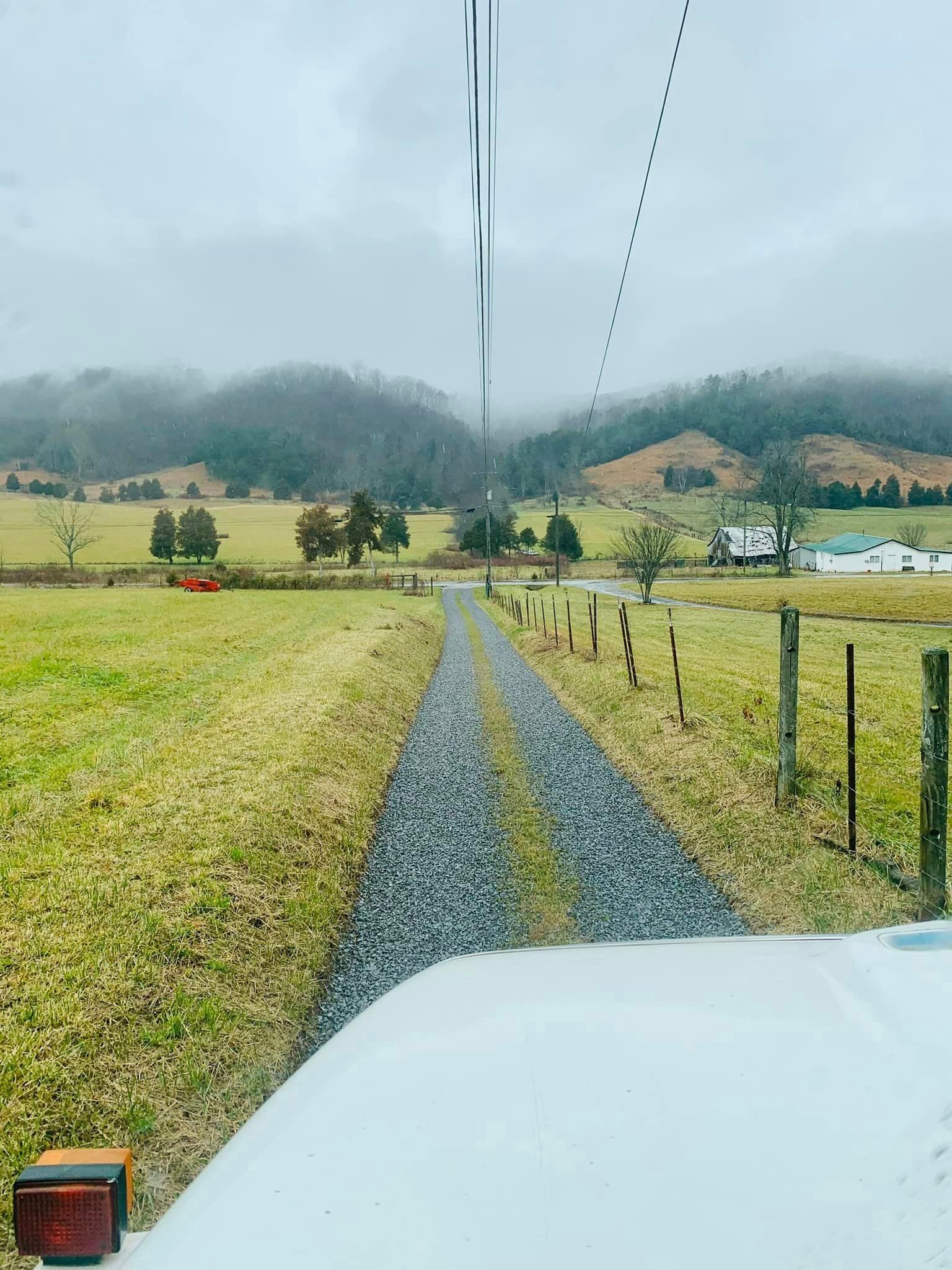 A gravel road going through a grassy field with mountains in the background.
