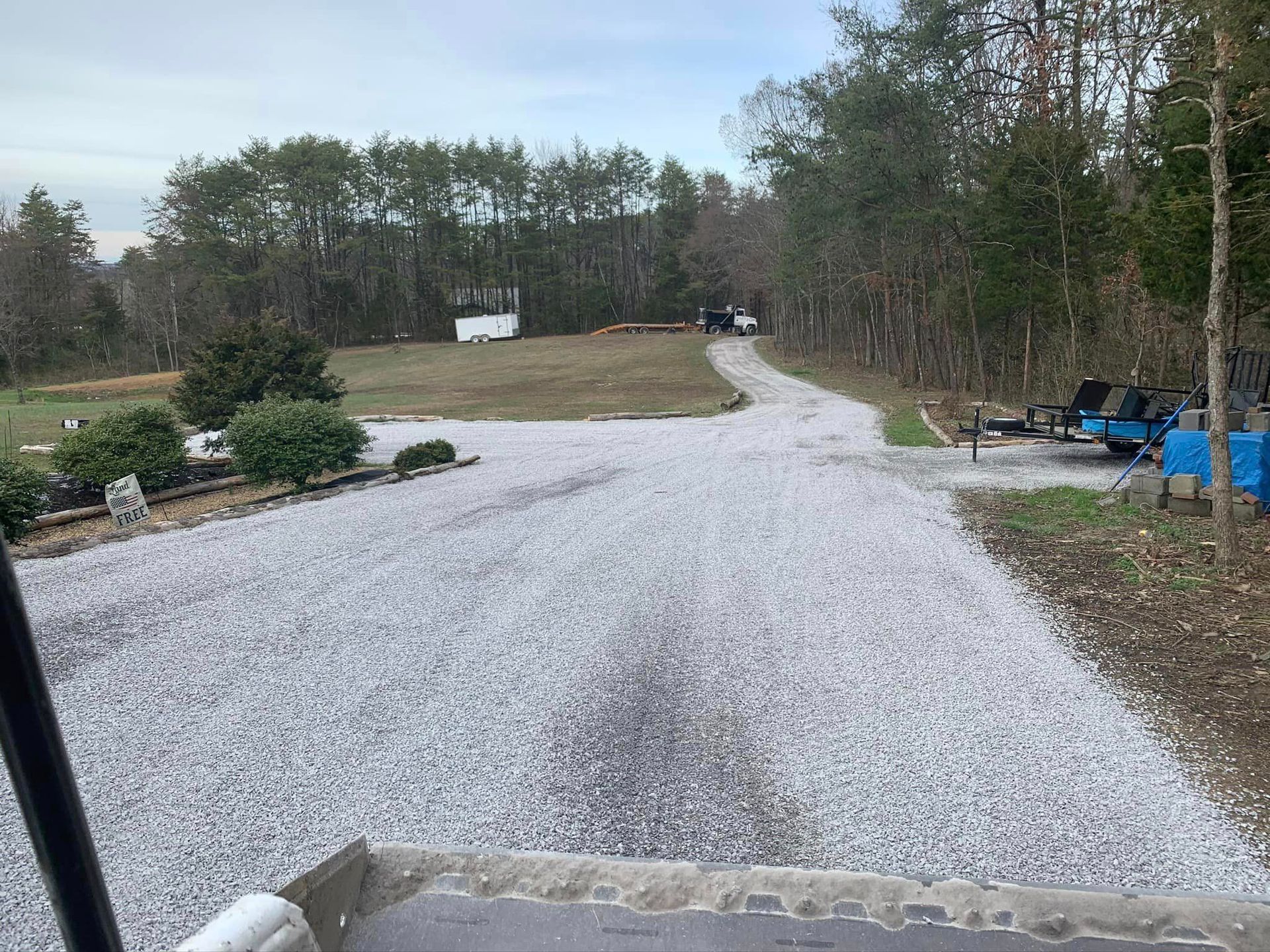 A gravel driveway leading to a house in the woods.