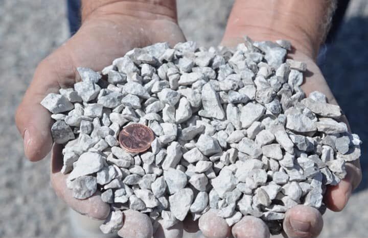 A person is holding a pile of gravel in their hands with a penny in it.