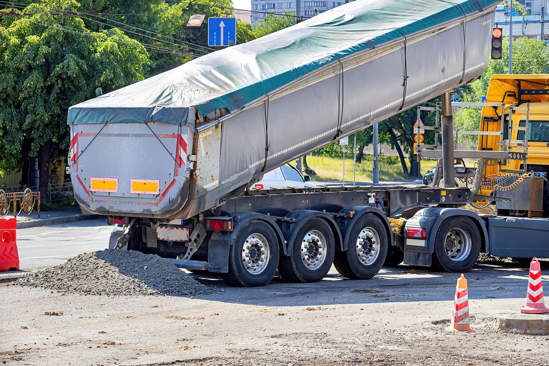 Gravel supplier services truck unloading gravel at busy urban construction site.
