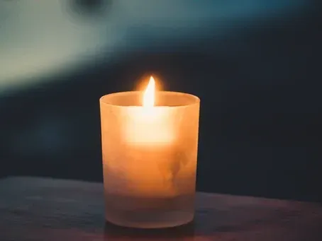 A lit candle in a glass on a wooden table.