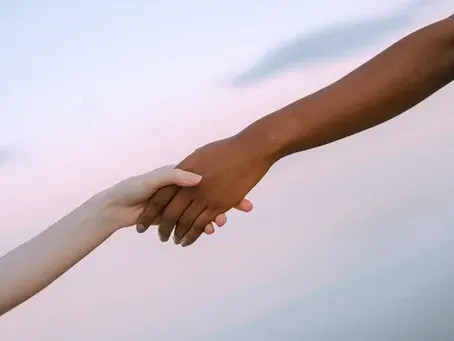 Two people are holding hands in front of a cloudy sky.