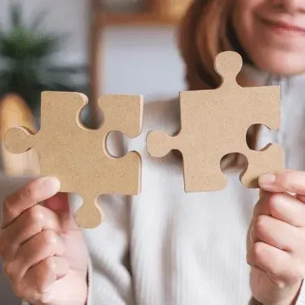 A woman is holding two cardboard puzzle pieces in her hands.