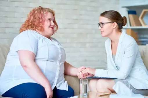 A woman is holding the hand of another woman while sitting on a couch.