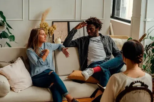 A man and a woman are sitting on a couch talking to a woman.