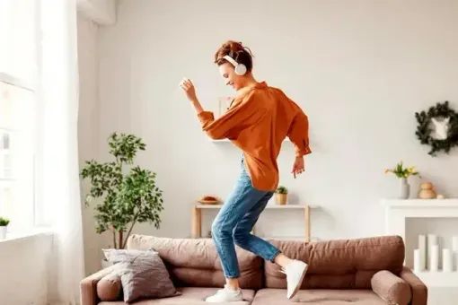 A man wearing headphones is jumping on a couch in a living room.