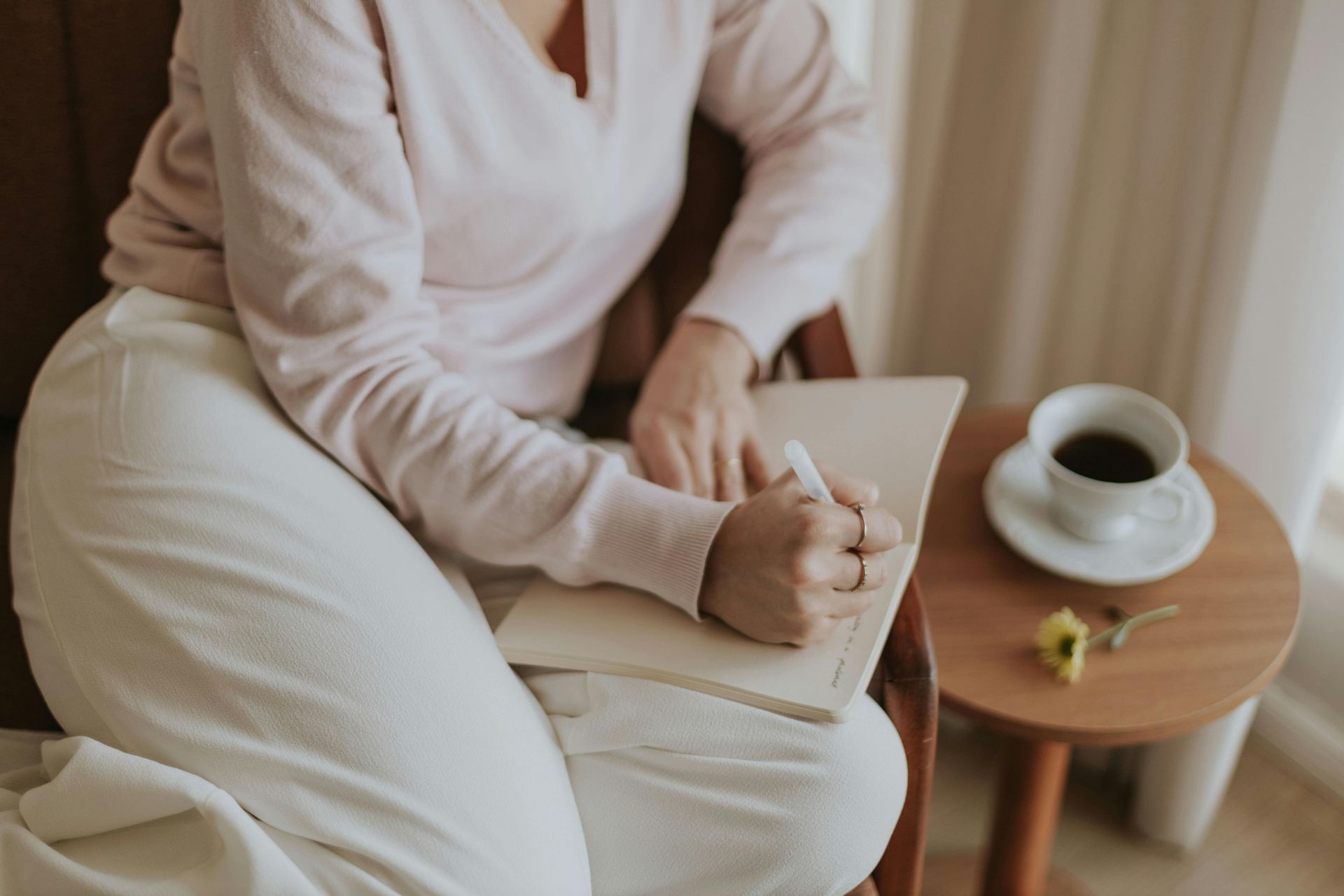 A woman is sitting at a table writing in a notebook with a pen.