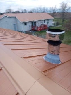 A roof with a chimney on it and a house in the background.