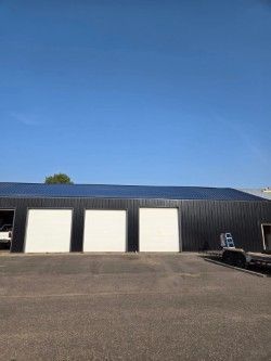 A black building with white garage doors and a blue sky in the background.
