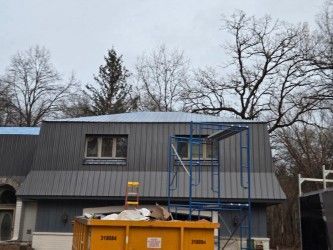 A house with a metal roof and a dumpster in front of it.