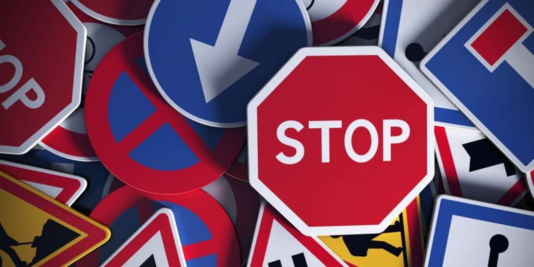 Close-up van een stapel verkeersborden, waaronder een rood stopbord en diverse blauwe en gele borden.