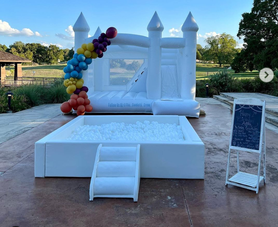 A white bouncy castle is sitting next to a white ball pit.