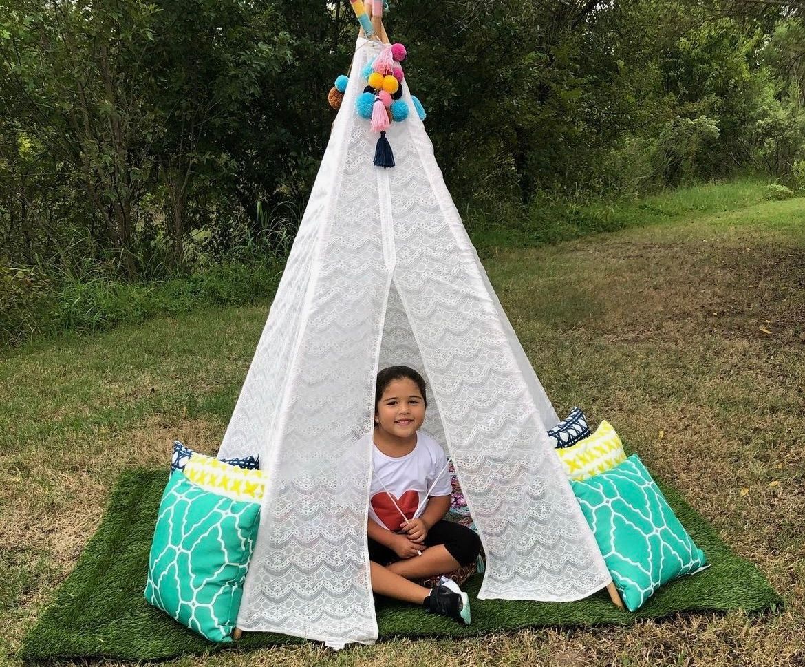 A little girl is sitting inside of a white teepee.