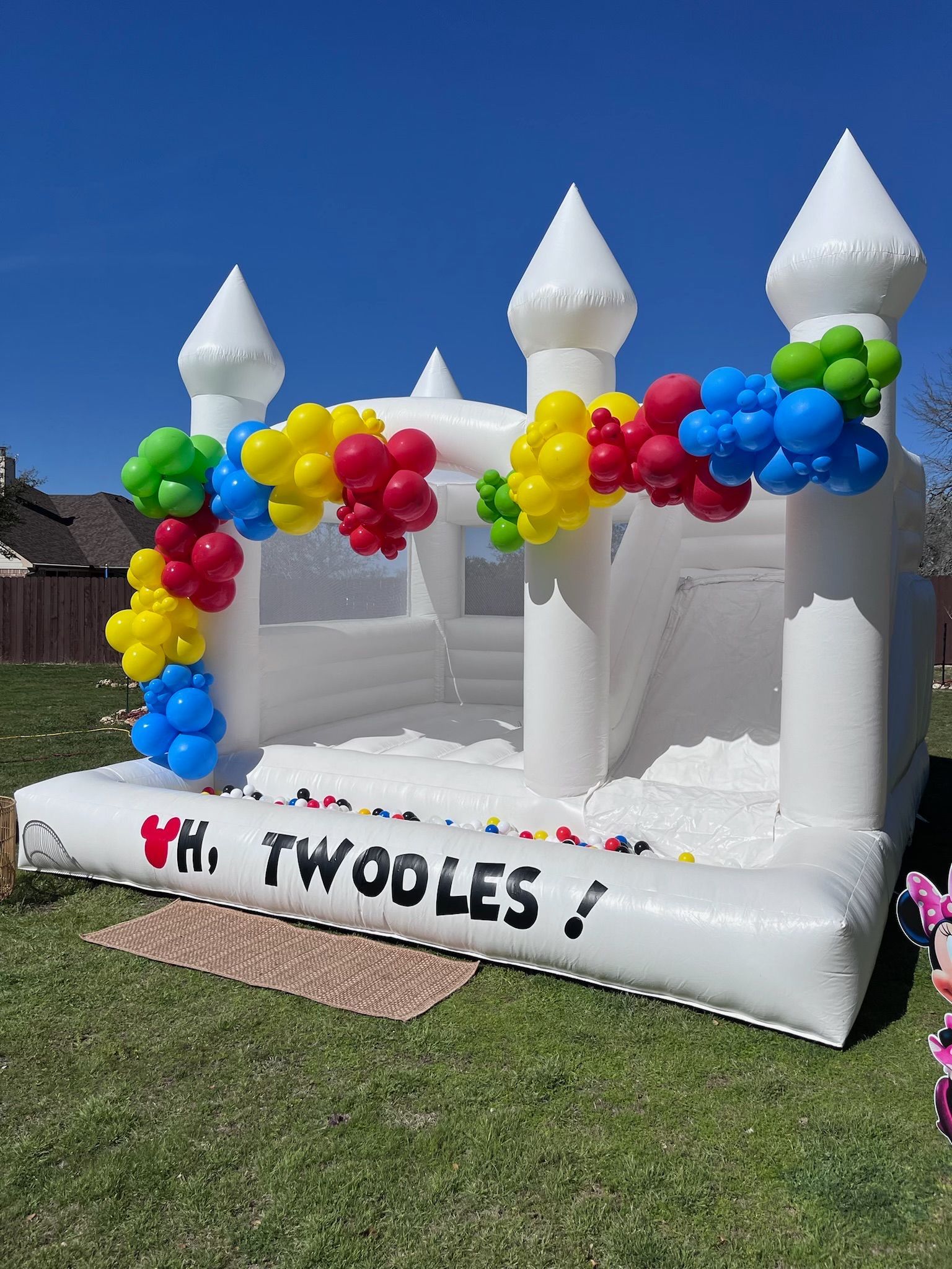 A white bouncy house decorated with balloons for a birthday party.