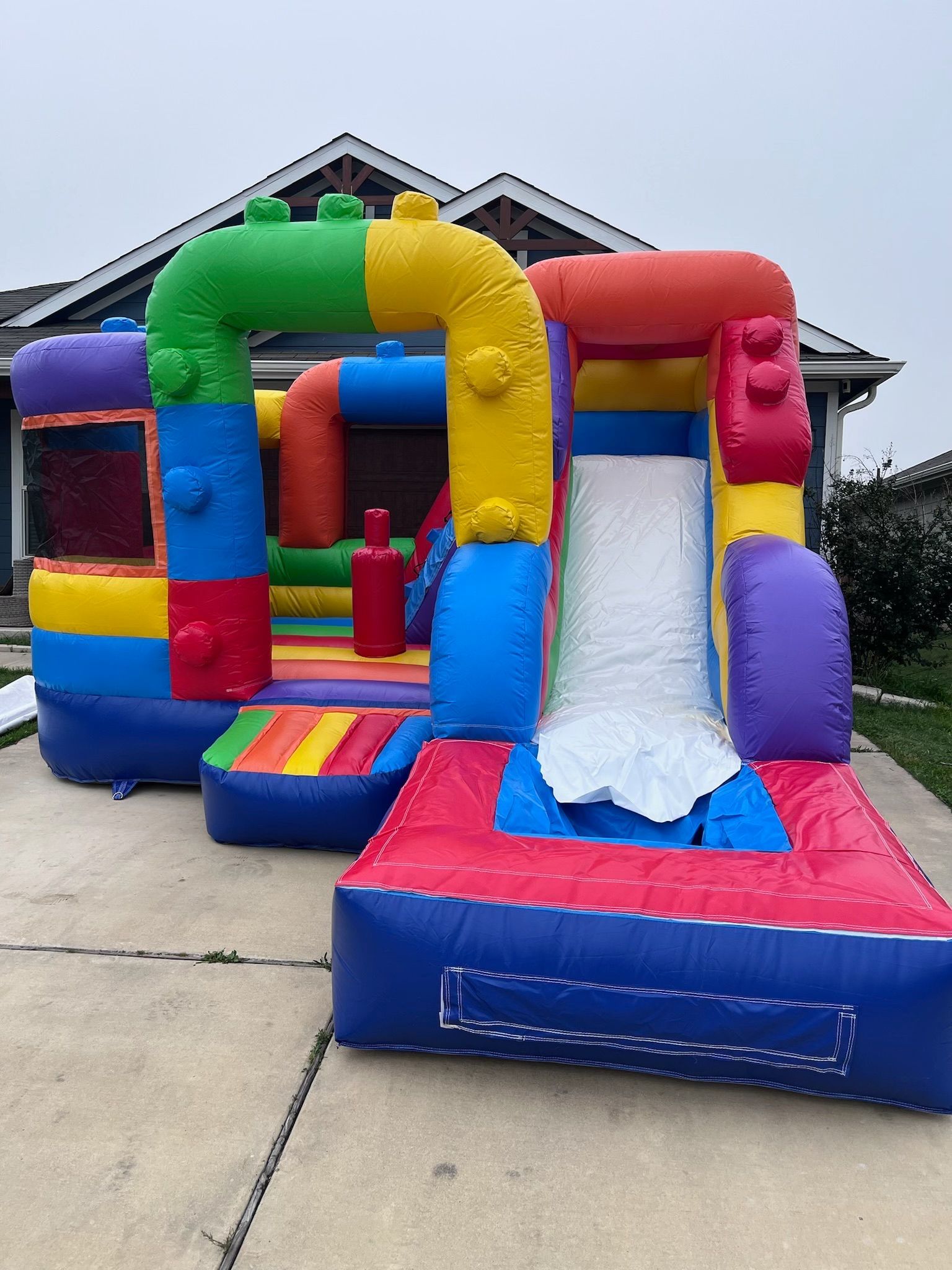 A colorful bouncy house with a slide in front of a house.