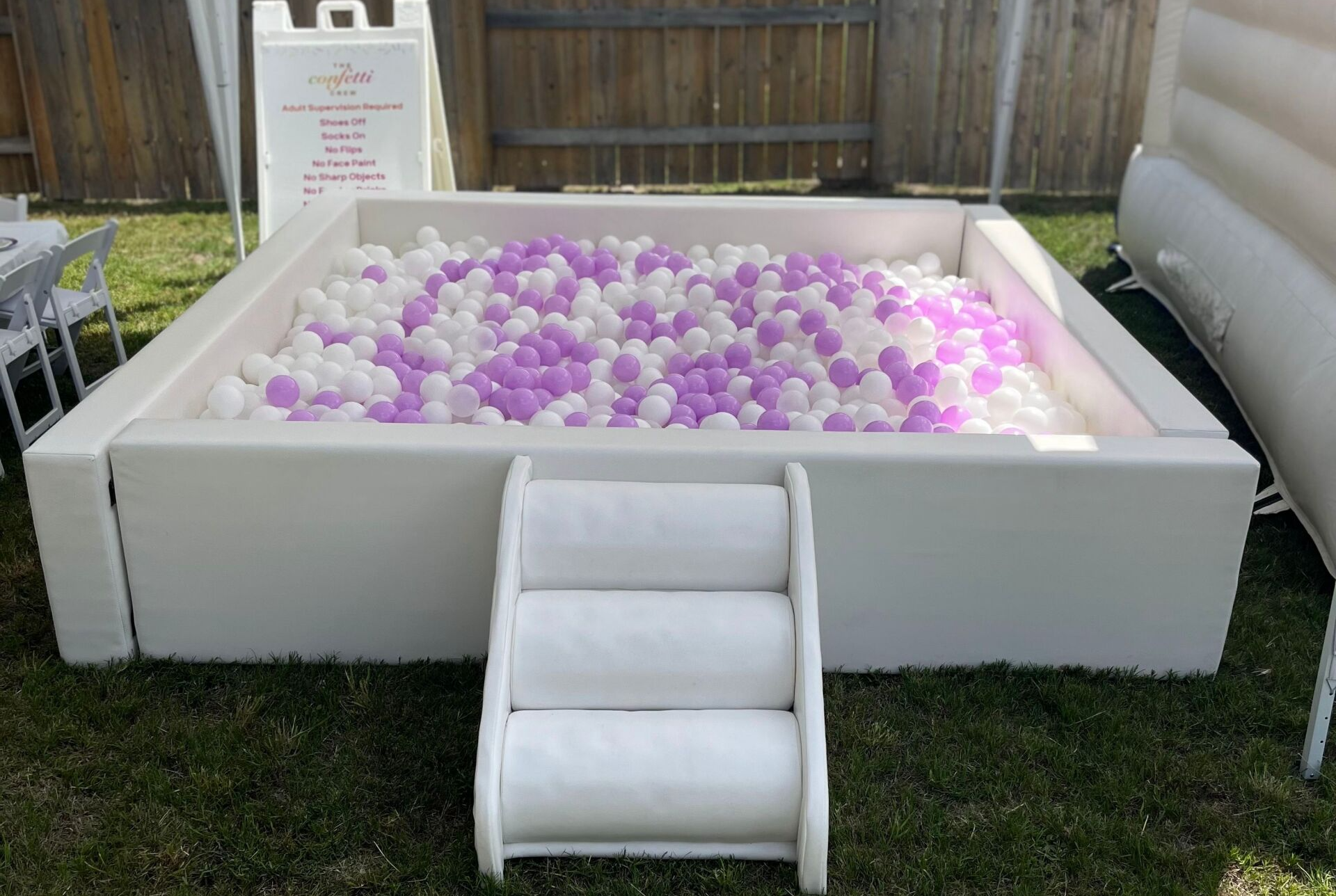 A white ball pit filled with purple and white balls and stairs.