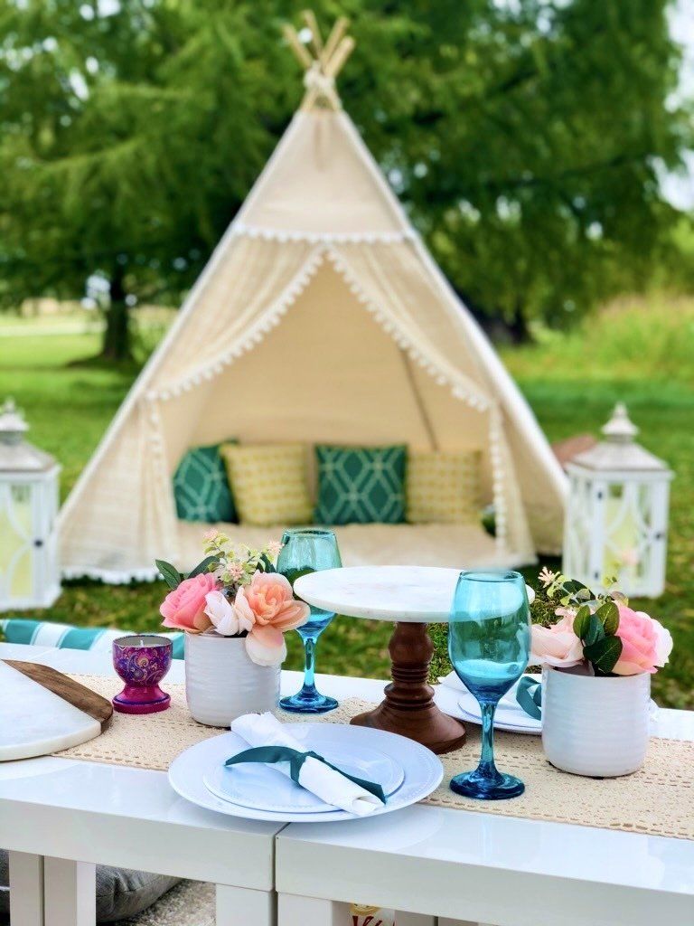 A table with plates , glasses , flowers and a teepee in the background.