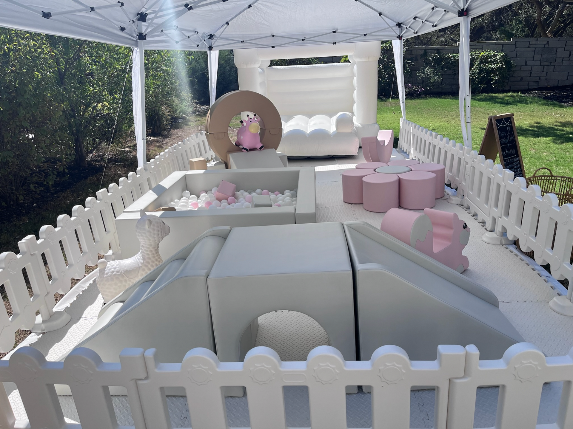 A white fence surrounds a play area with a bouncy castle.