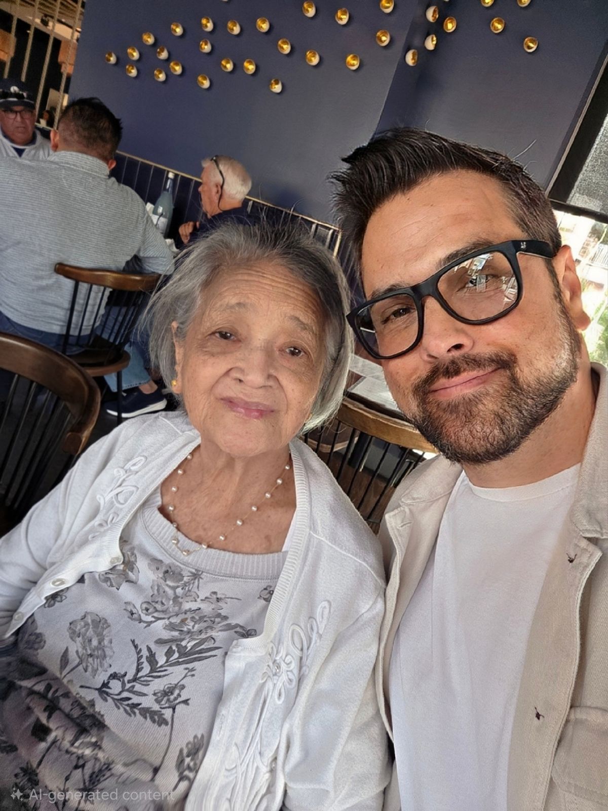 Del and his mom smiling for a selfie together inside a restaurant with a dark blue wall in the background.