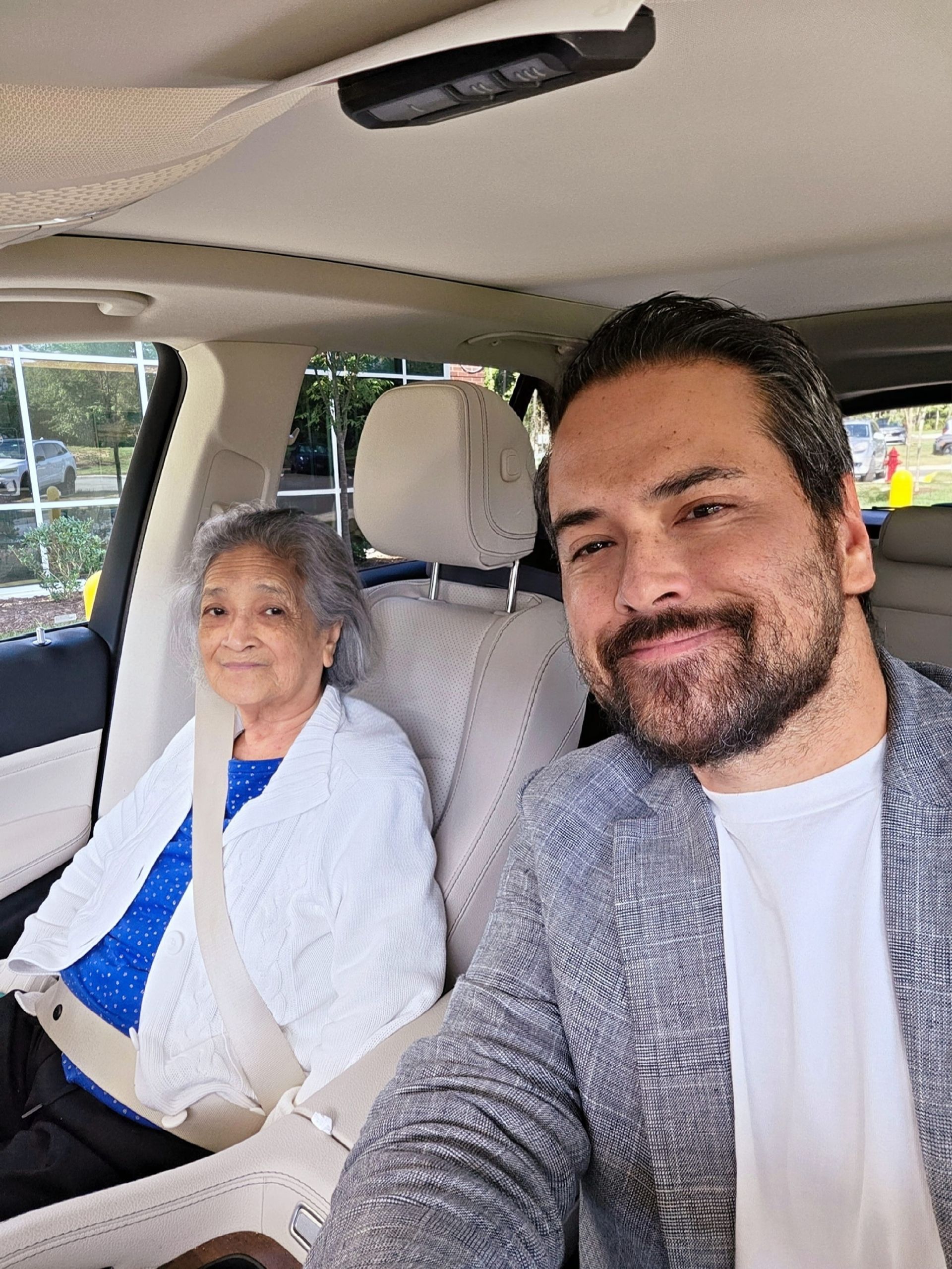 Del and his mom are smiling inside a car, seated in the passenger and driver seats.
