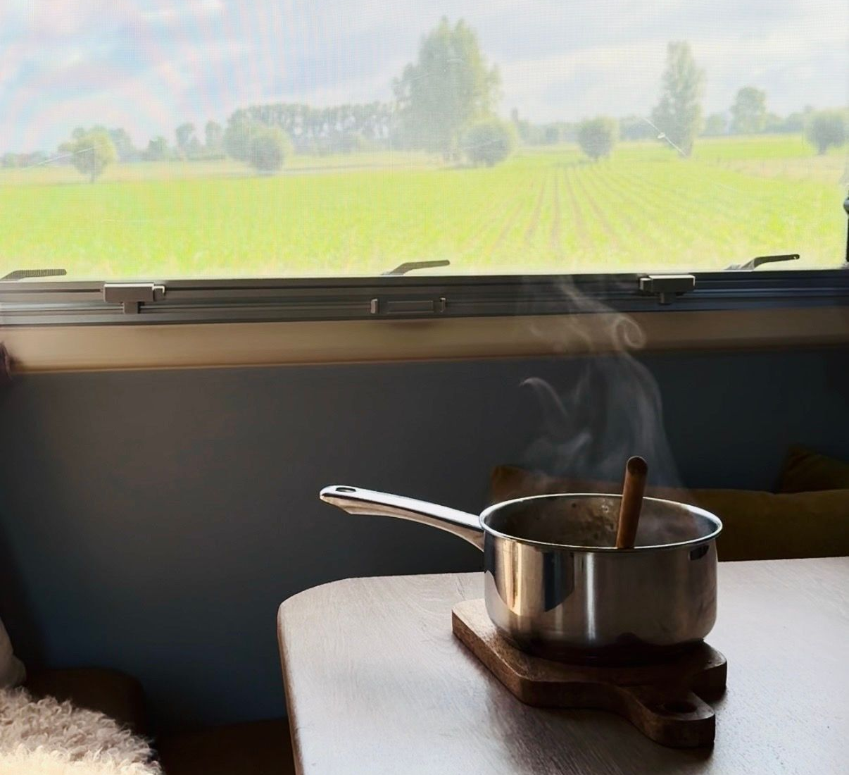 Steaming pot on a stove by a window overlooking a green field