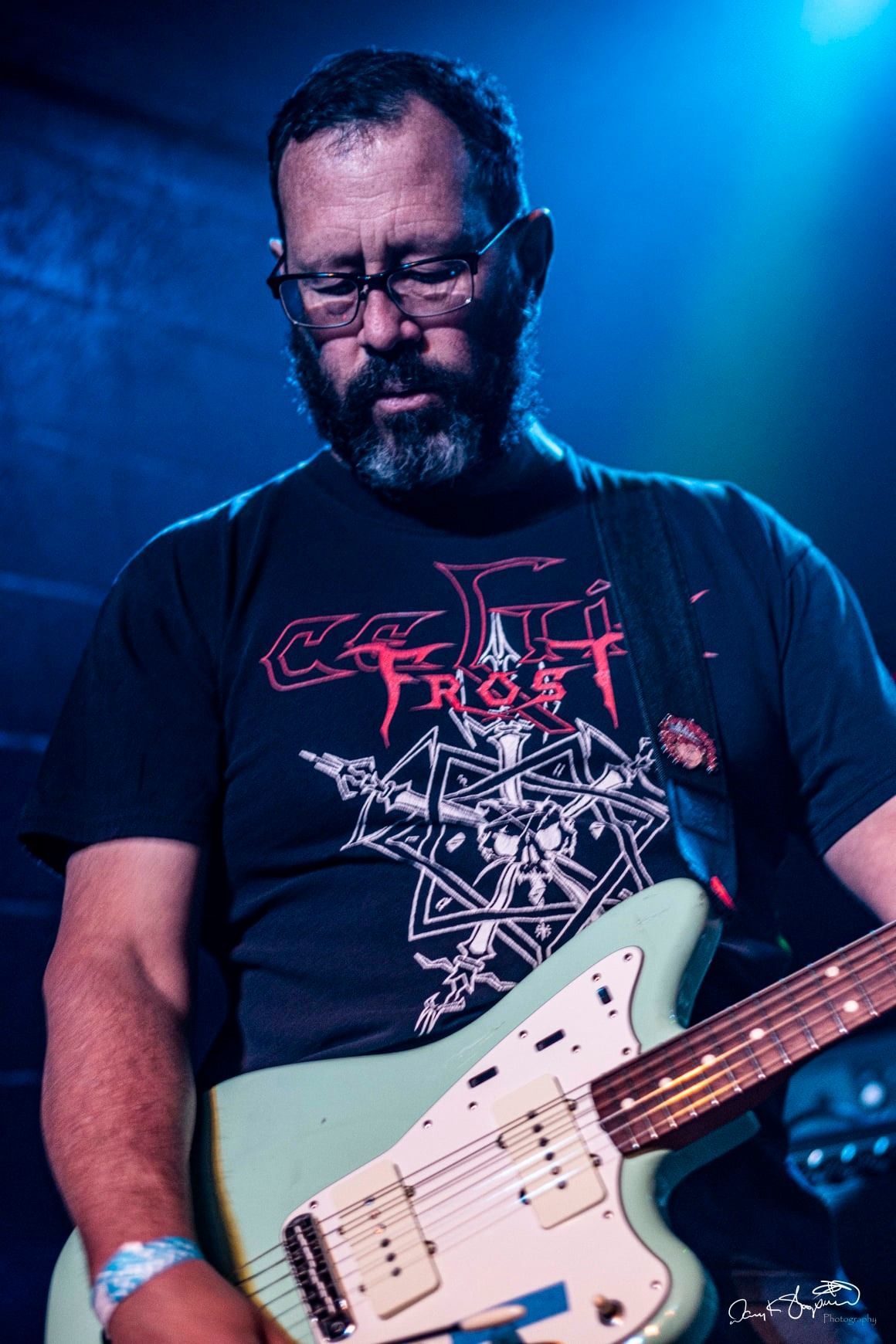 Man playing a mint green electric guitar, wearing a Celtic Frost t-shirt and glasses.