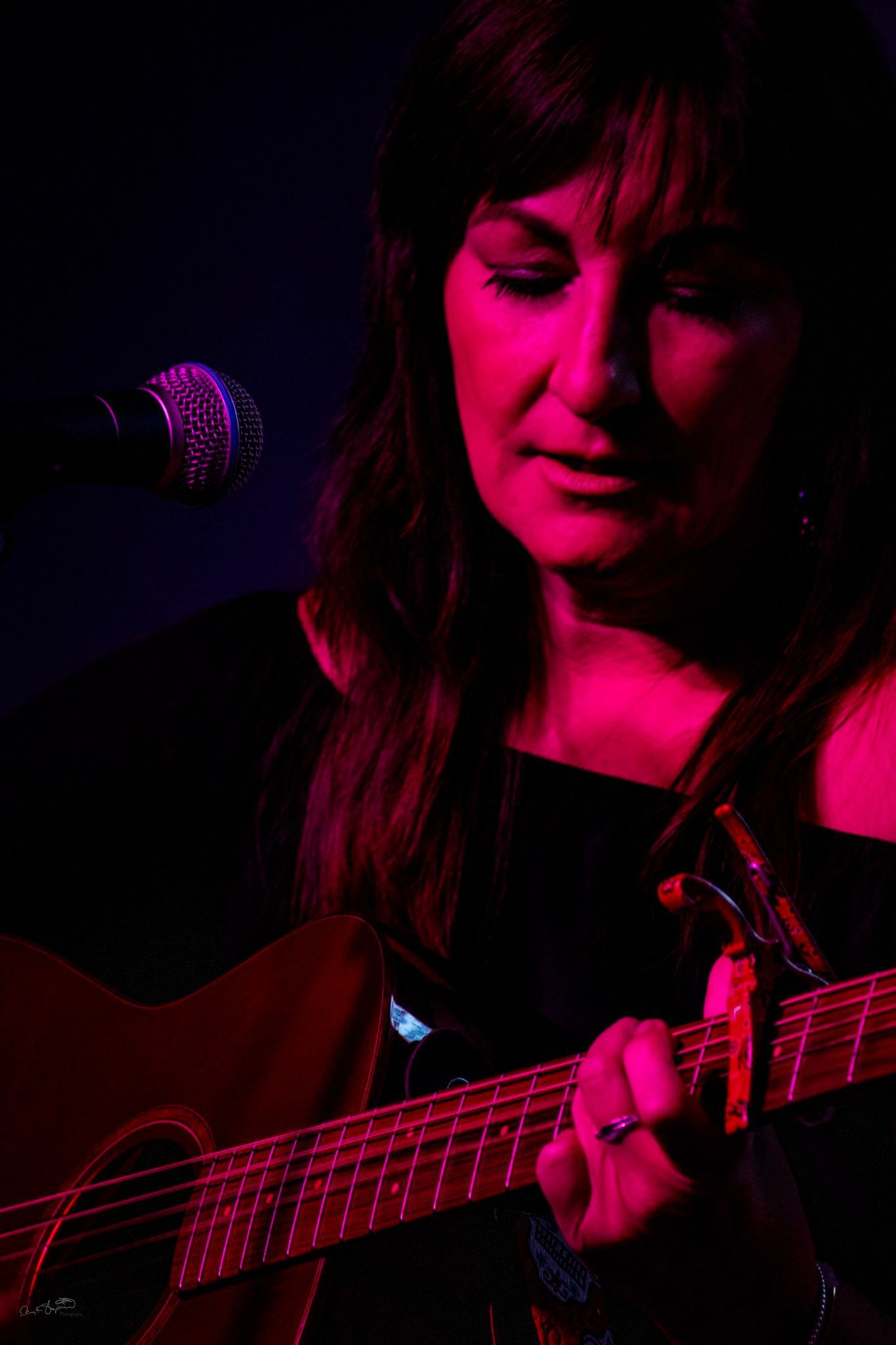 Woman playing acoustic guitar under pink stage lighting.