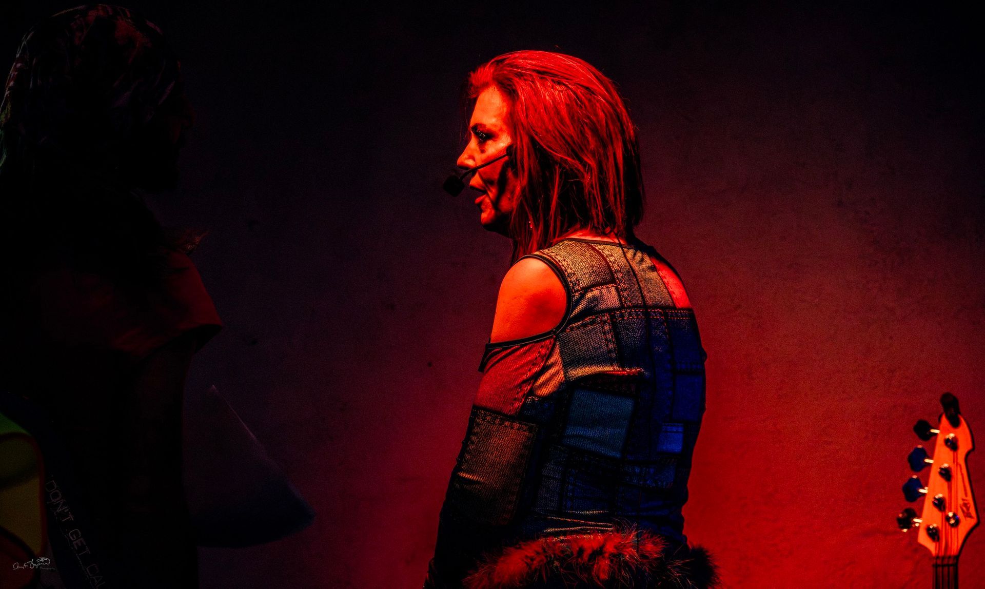 Woman with red hair on stage, wearing a black outfit with cutouts. Stage lit with red and orange light.