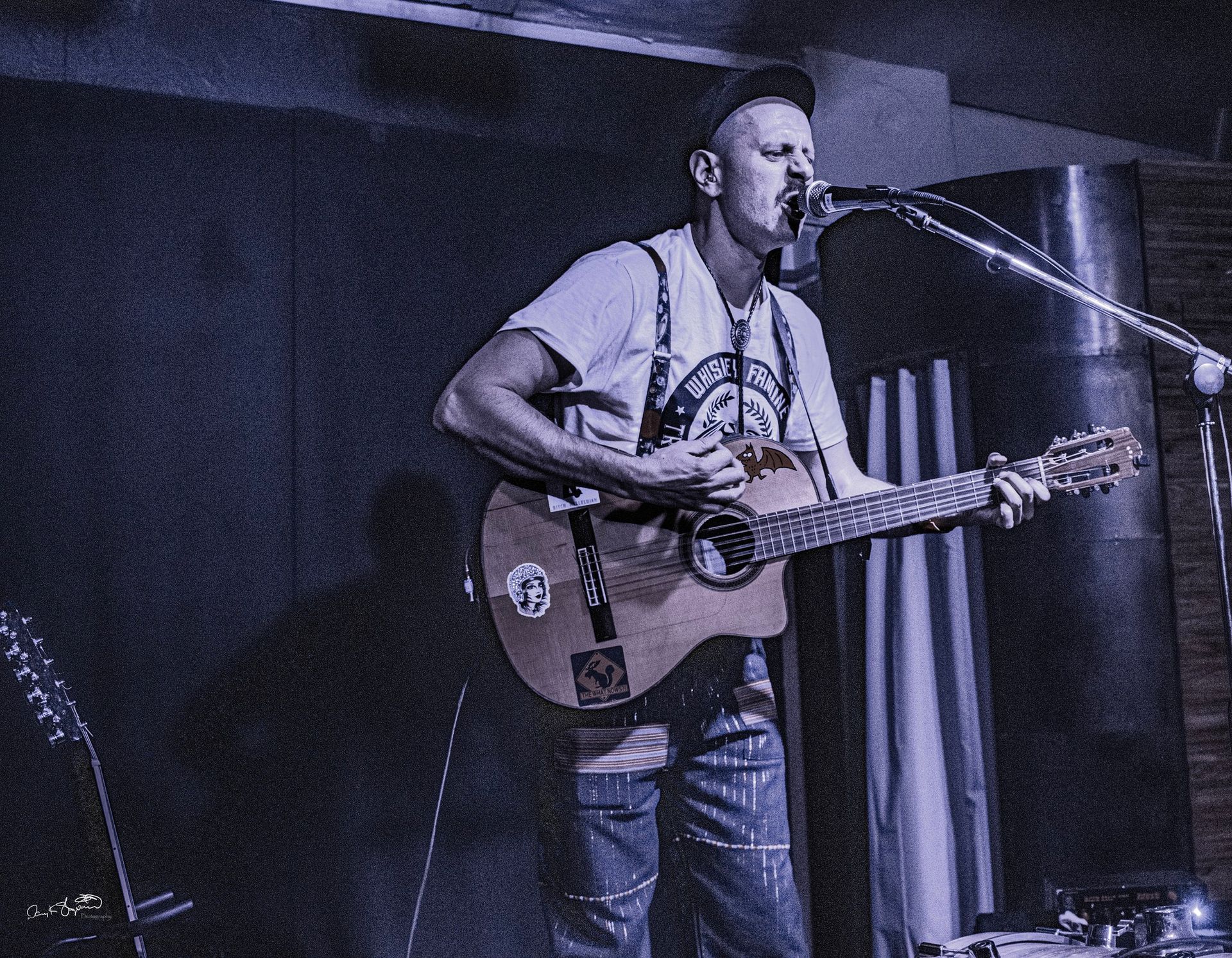Man playing guitar and singing into a microphone onstage under blue lights.