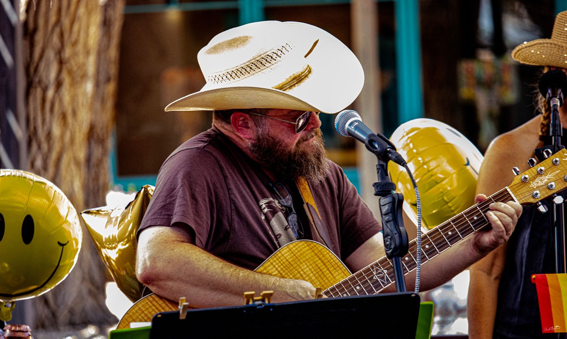 Man in cowboy hat plays acoustic guitar on stage, singing into a microphone.